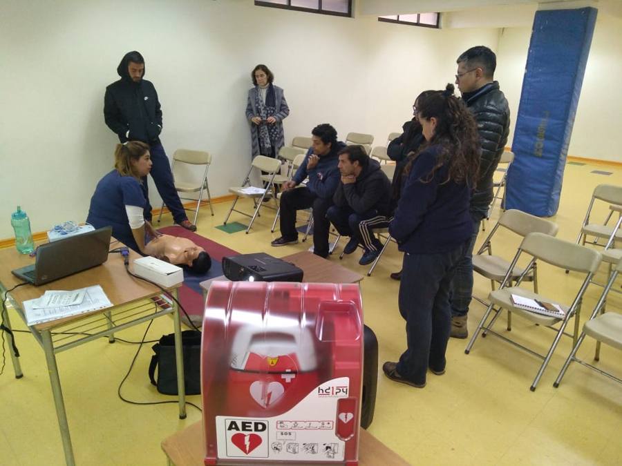 Práctica de reanimación en el gimnasio de un colegio con el gabinete del DEA en primer plano